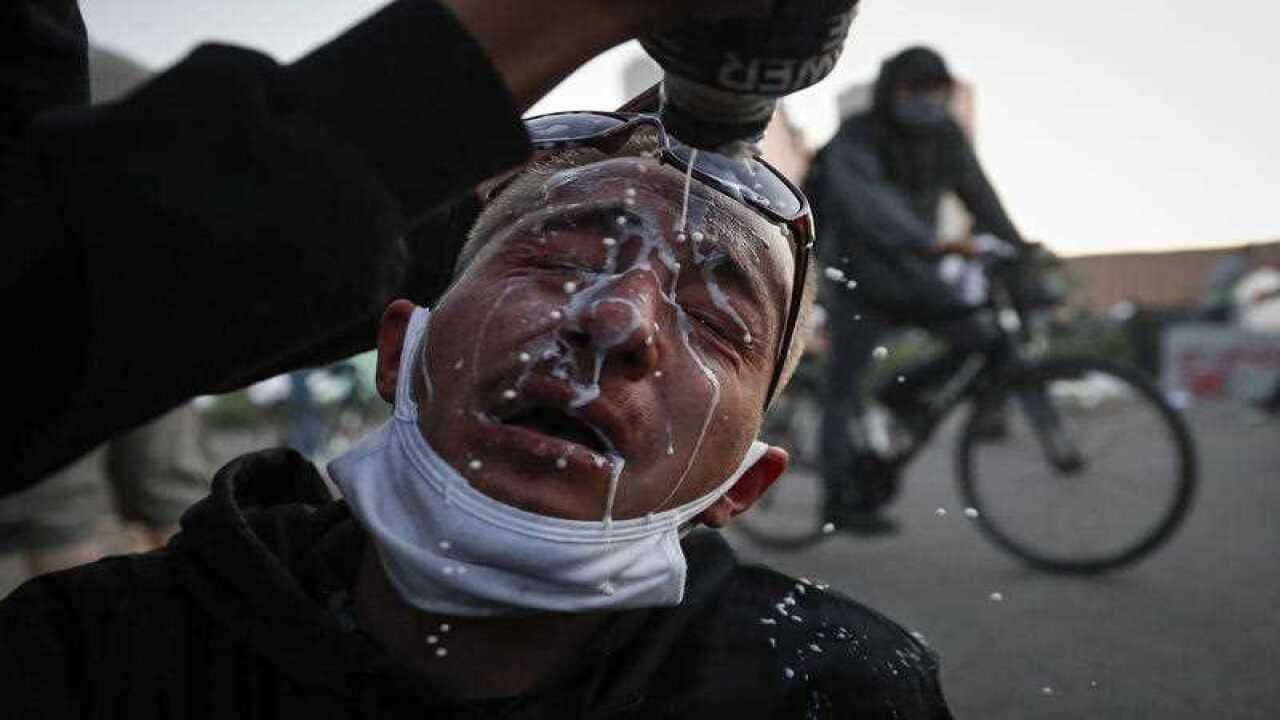 A protester is assisted with a solution to help neutralize the effects of tear gas fired by police outside the Minneapolis 5th Police Precinct