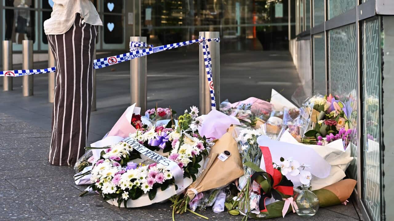 A woman looks at flowers and wreaths outside the shopping centre where six people were killed.