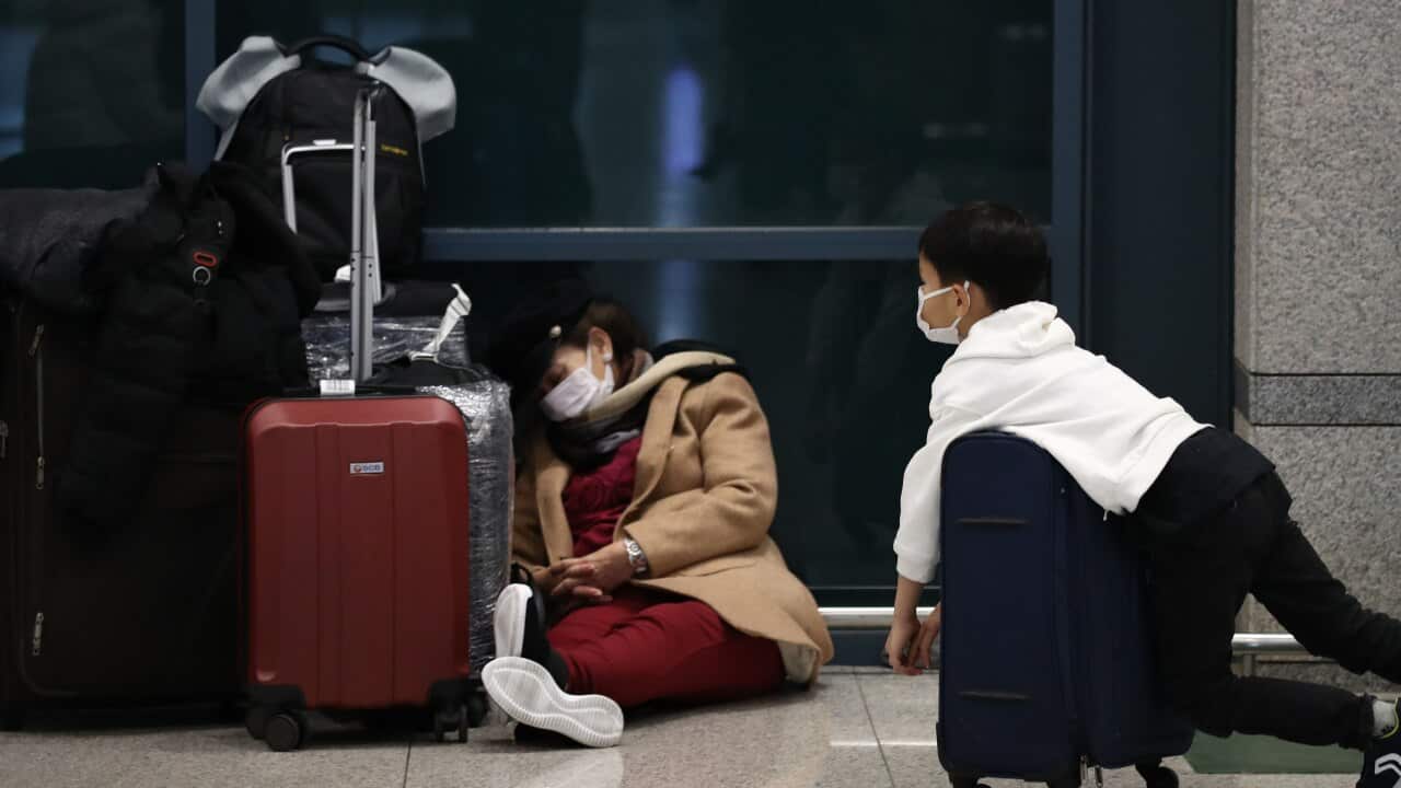 Travellers wearing masks rest on the floor of Incheon International Airport in South Korea.