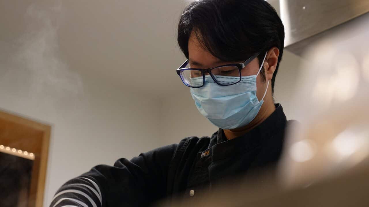 A young man wearing a mask working in a kitchen