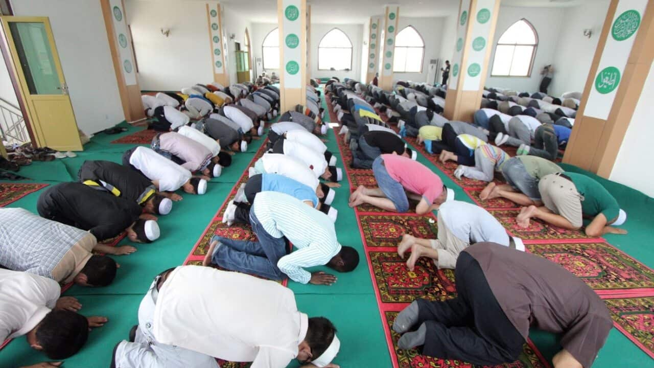 An African Muslim, center, kneels and bows among Chinese Muslims as they attend an Eid al-Fitr morning prayer