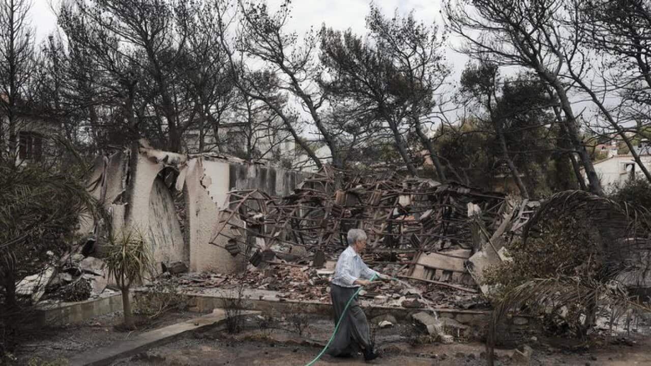 A woman sprays water outside her house that was damaged in the wildfires near the village of Neos Voutzas near Athens,