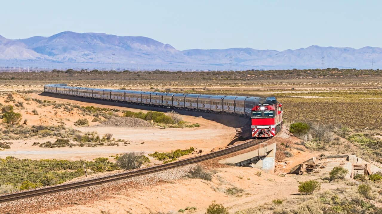 Long distance luxury passenger train with red engine in outback South Australia with Flinders Ranges backdrop