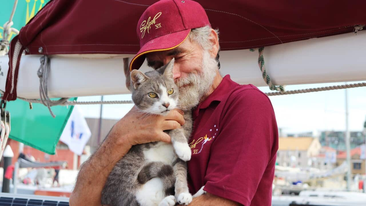 A man in a maroon cap and polo shirt holds a cat on the boat