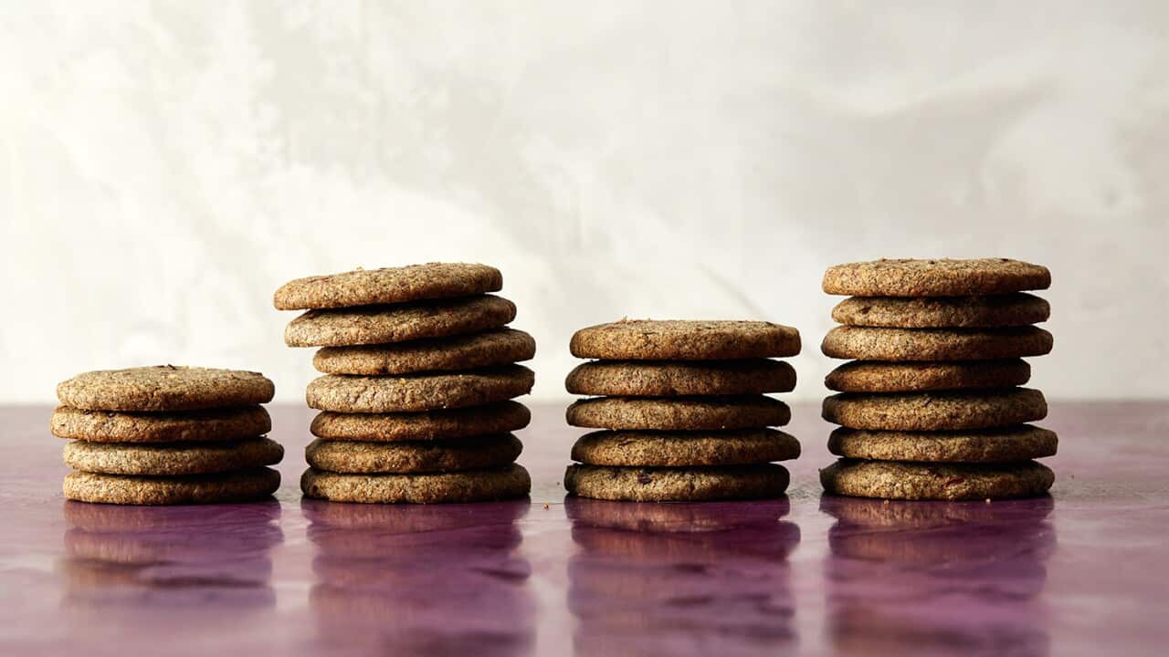 Four different height stacks of thin brown cookies sit on a pink surface, in front of a cream background.
