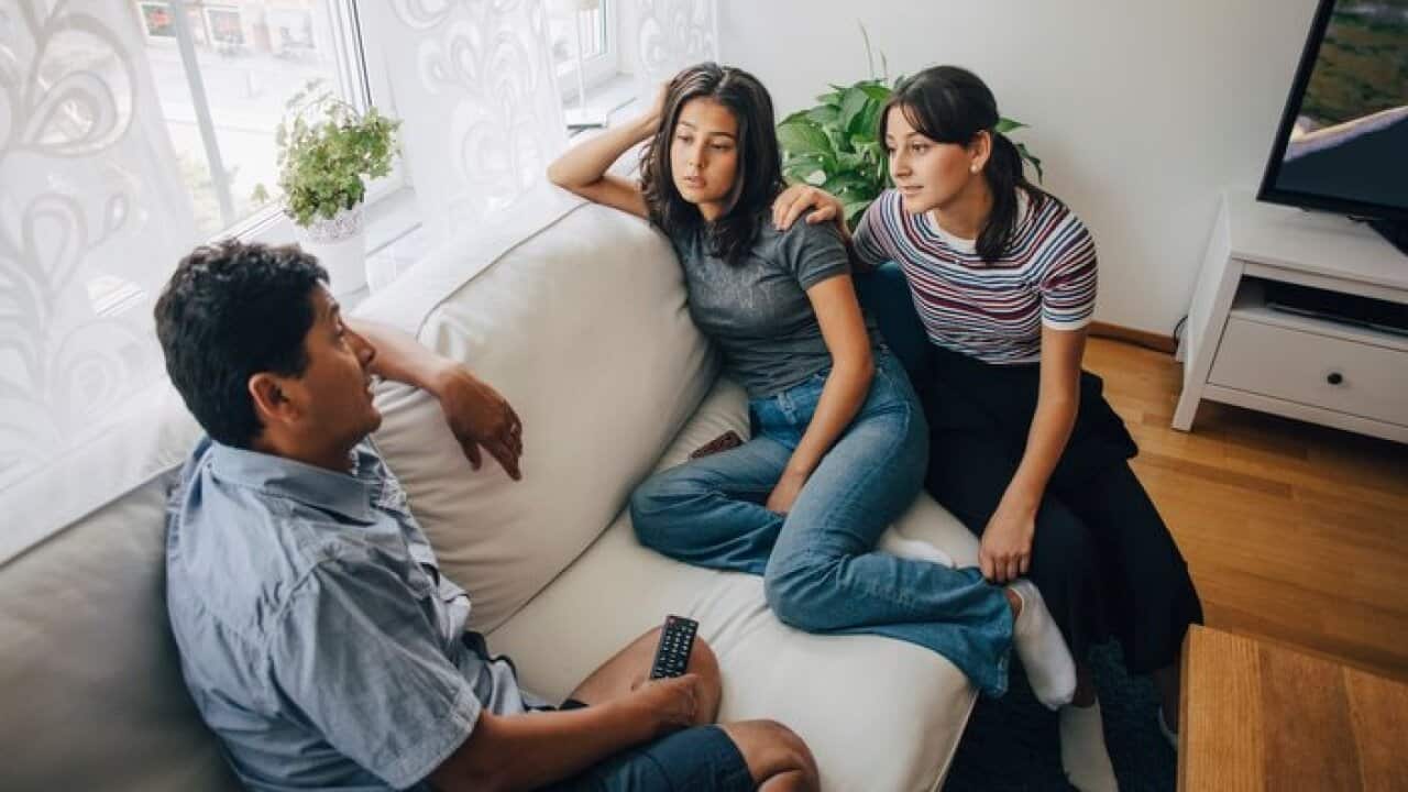 Daughters listening to father while sitting on sofa at home