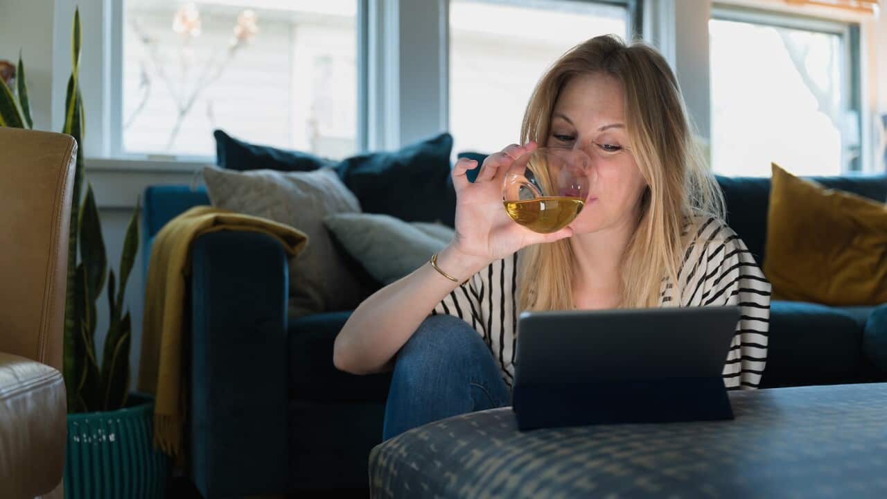 Woman drinking wine and looking at tablet at home