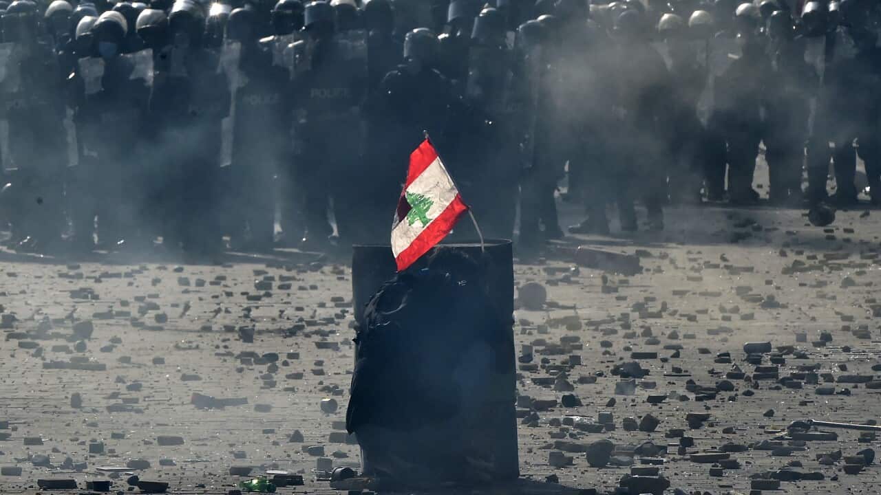 An anti-government protester carries a Lebanese flag as he protects himself behind an iron barrel during a protest in Beirut