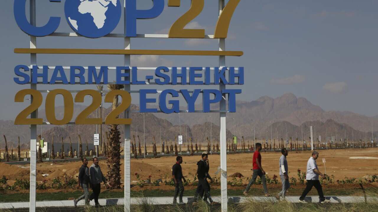 Workers walk past signage promoting this year’s United Nations global summit on climate change, known as COP27, South Sinai, Egypt (AAP).