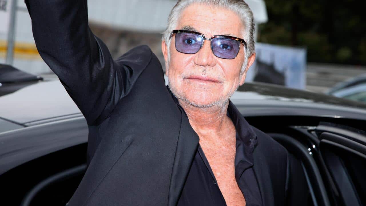 A man wearing purple-tinted sunglasses waving.