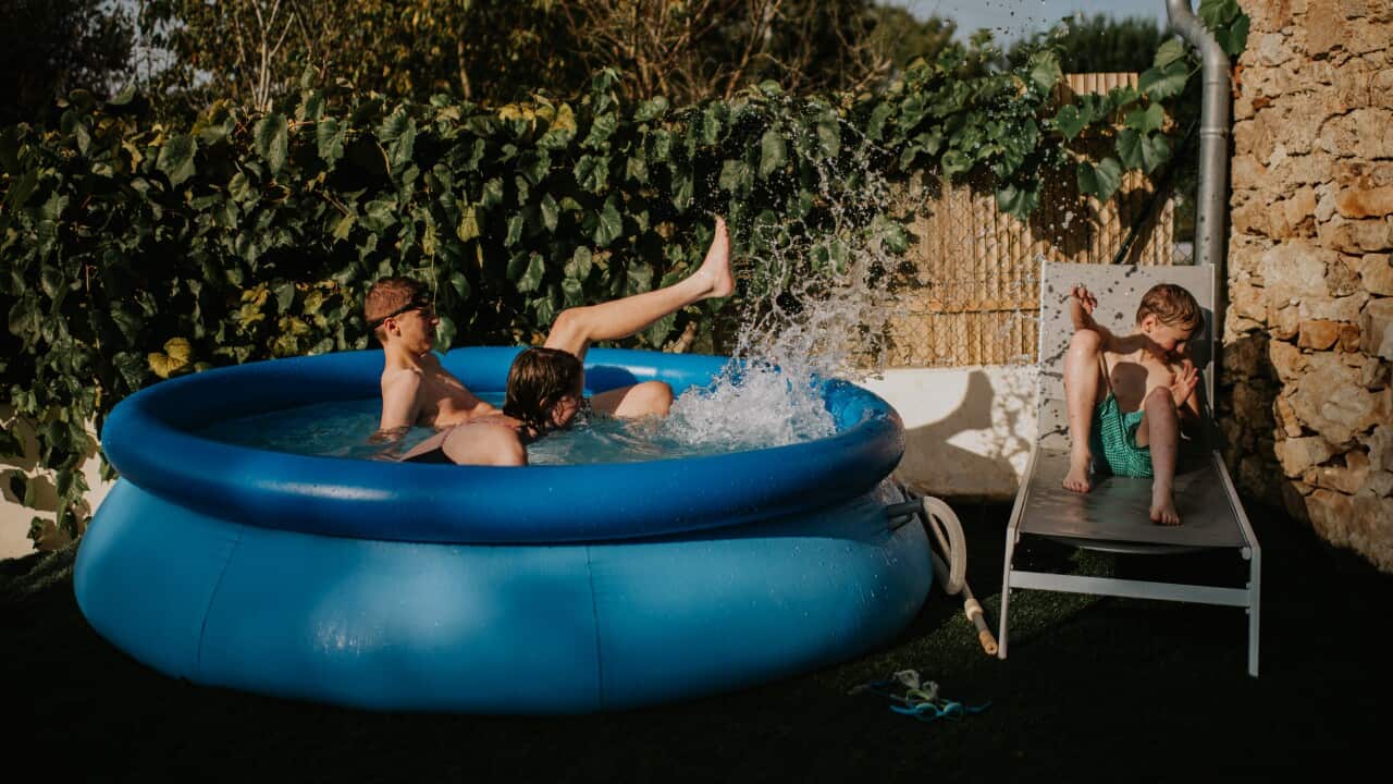 Two kids in an inflatable pool and one sitting on a deckchair