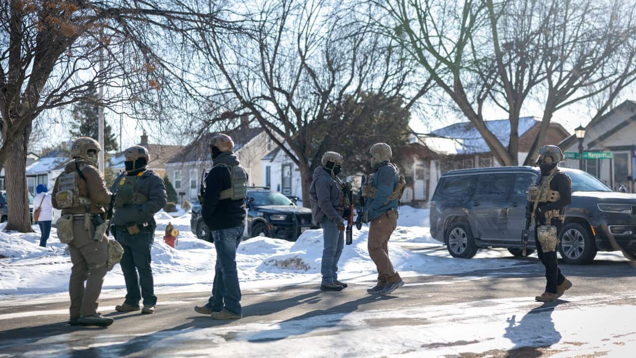 Immigration agents wearing helmets, vests and carrying guns standing on a street.