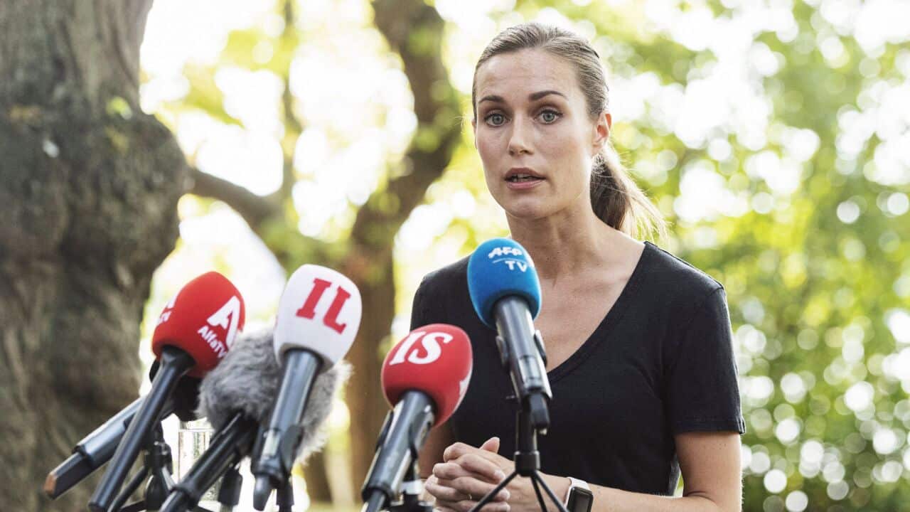 A brunette woman in her 30s wearing a black top speaks at an outdoors press conference