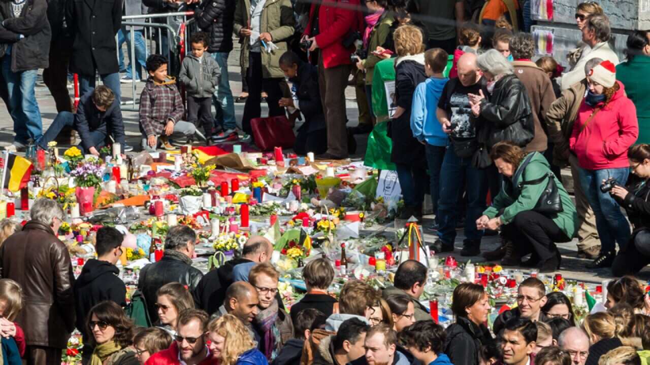 People gather around floral tributes at a memorial site in Brussels