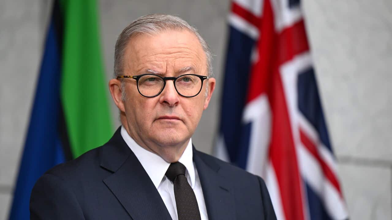 A man wearing a suit and glasses standing in front of two flags