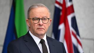 A man wearing a suit and glasses standing in front of two flags