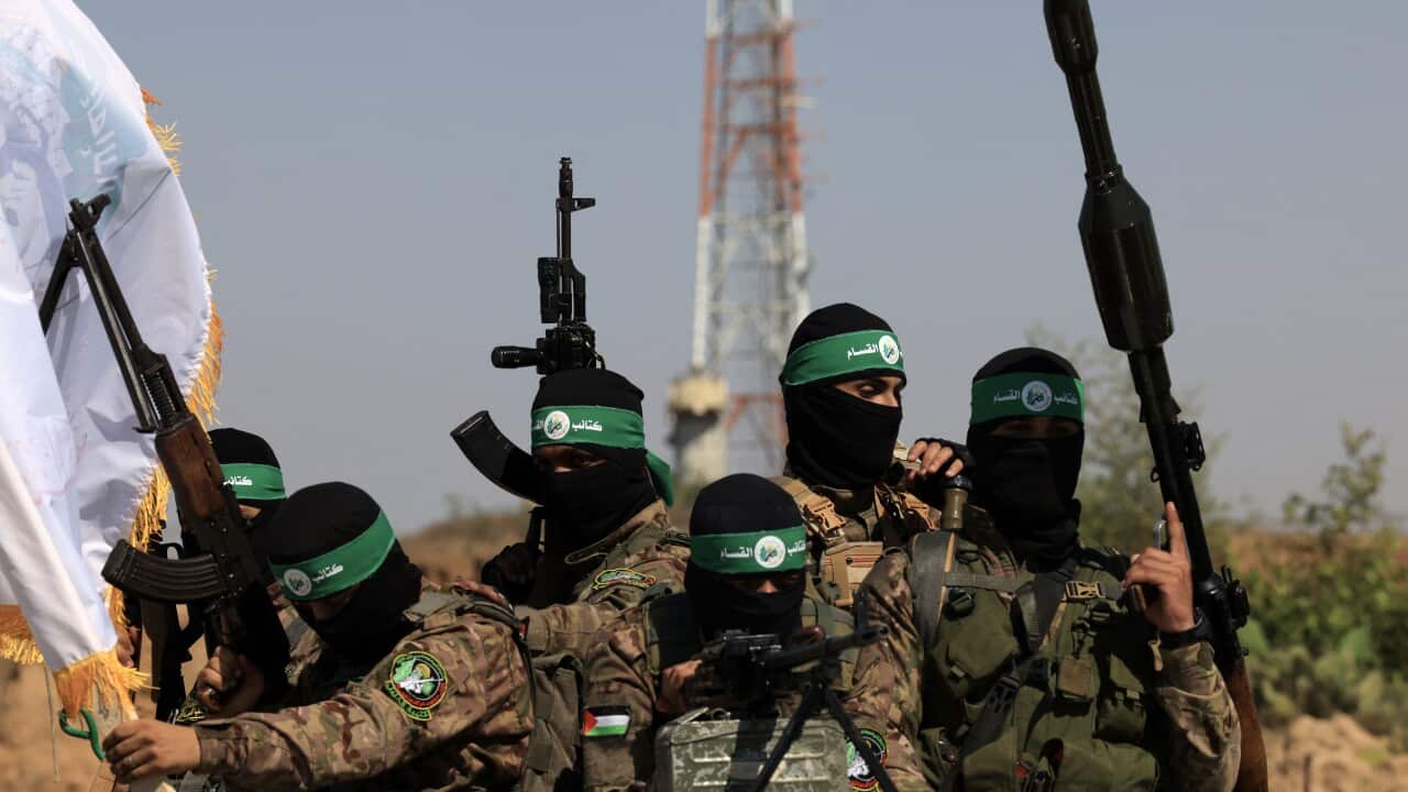 A group of militants wearing black face masks carry weapons while riding in the back of a truck