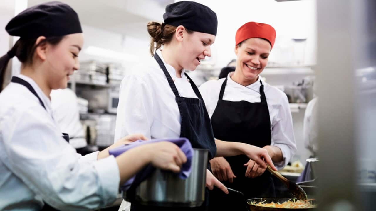 Teacher watching female chef students cooking food in commercial kitchen