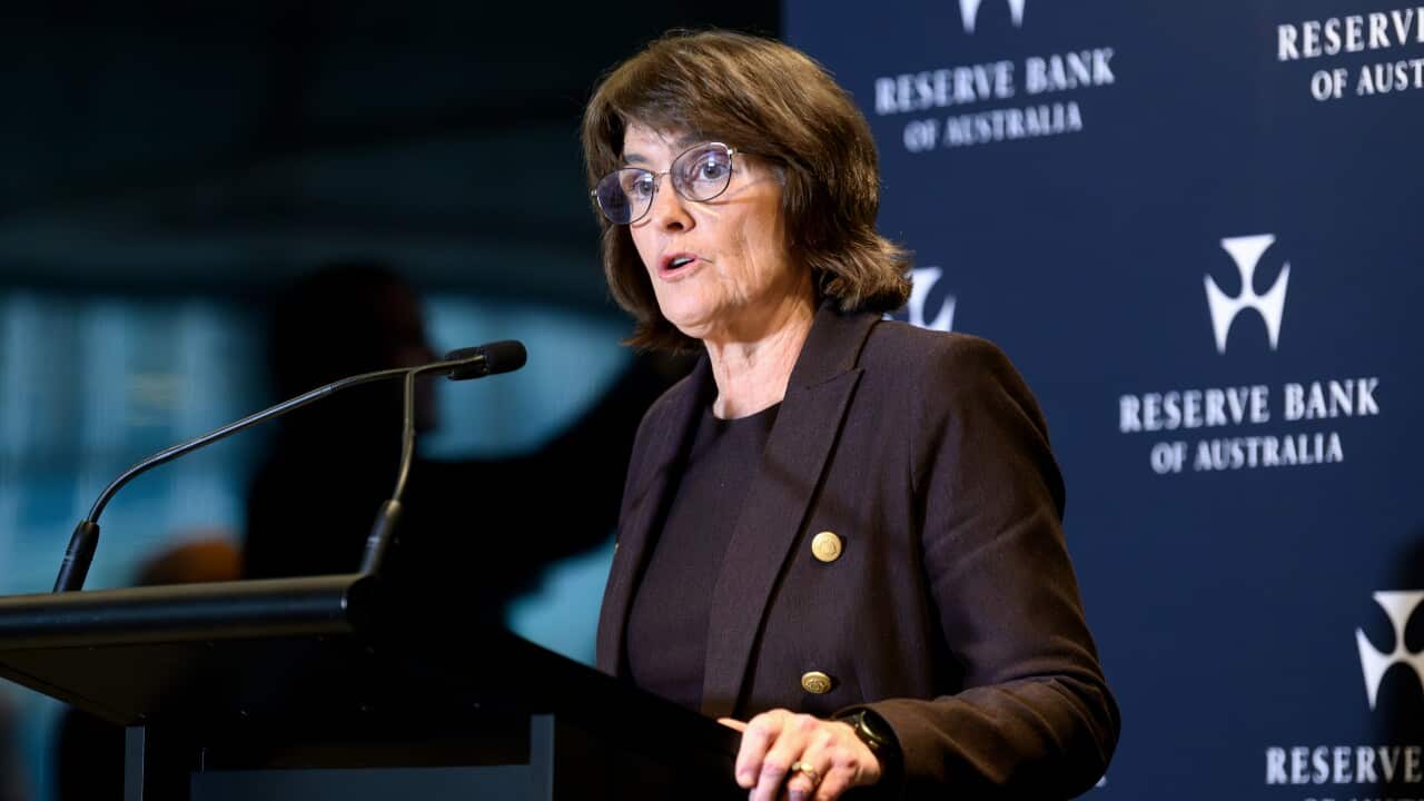 A woman in a dark suit and glasses giving a speech at a podium