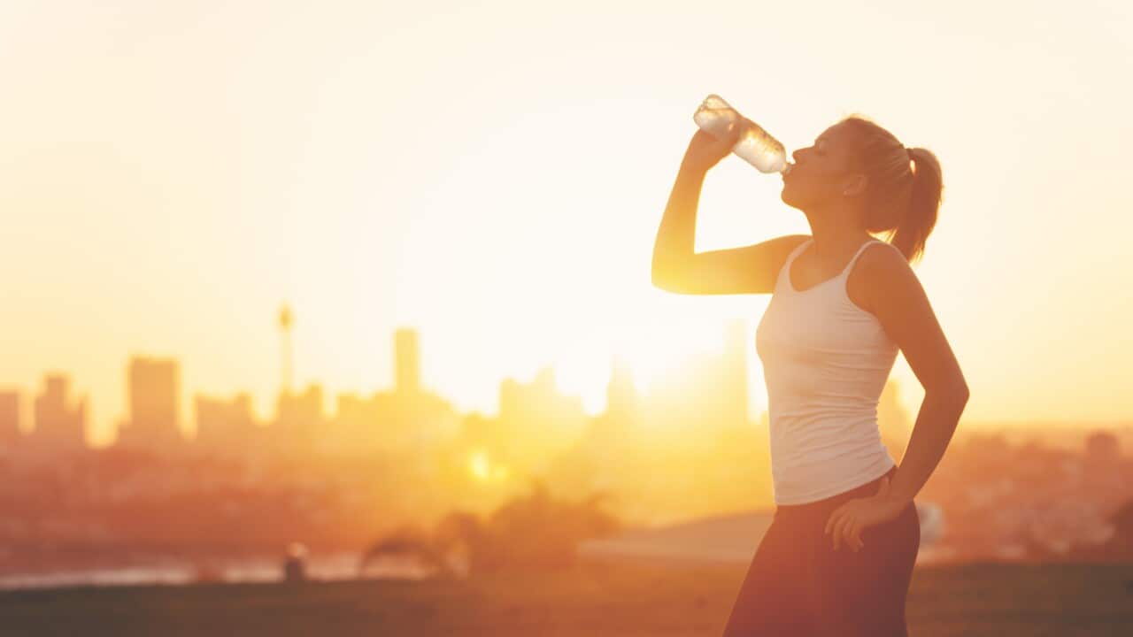 Silhouette of a woman drinking form a cold water bottle.