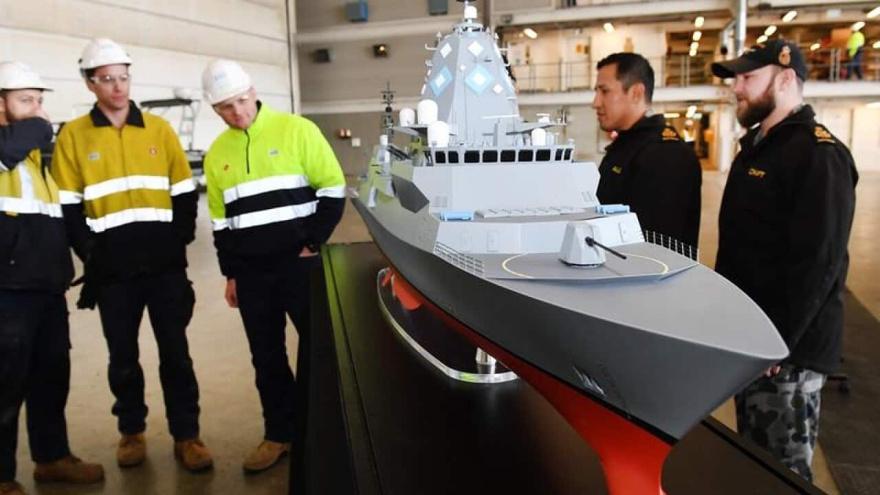 Workers stand around the model of a ship