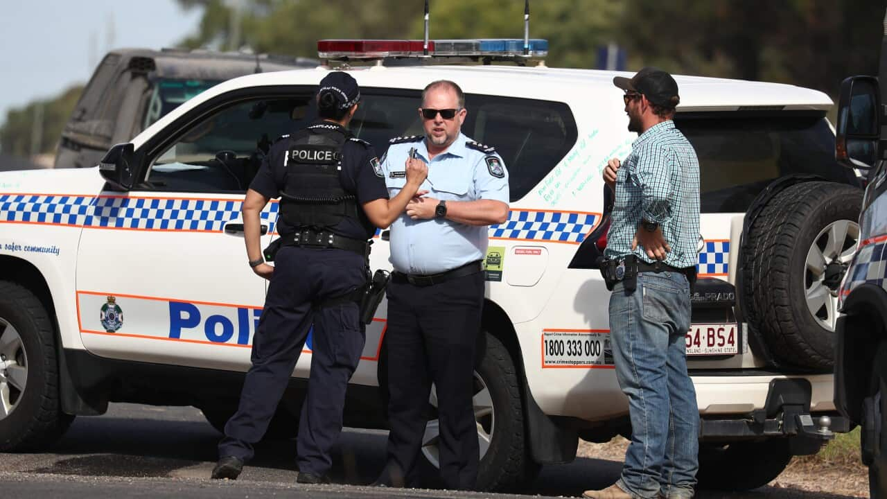 Police officers standing on the road in front of a vehicle that is parked.