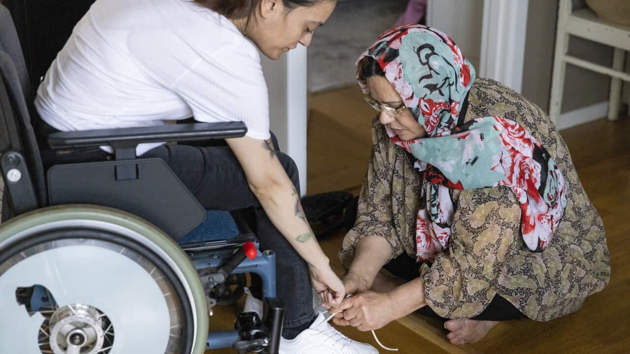 Mother tying shoelace of daughter sitting on wheelchair at home
