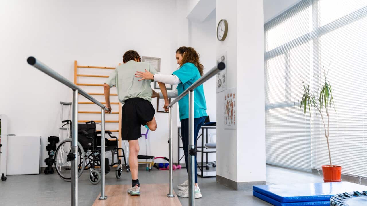 Young man uses parallel bars in a rehab center