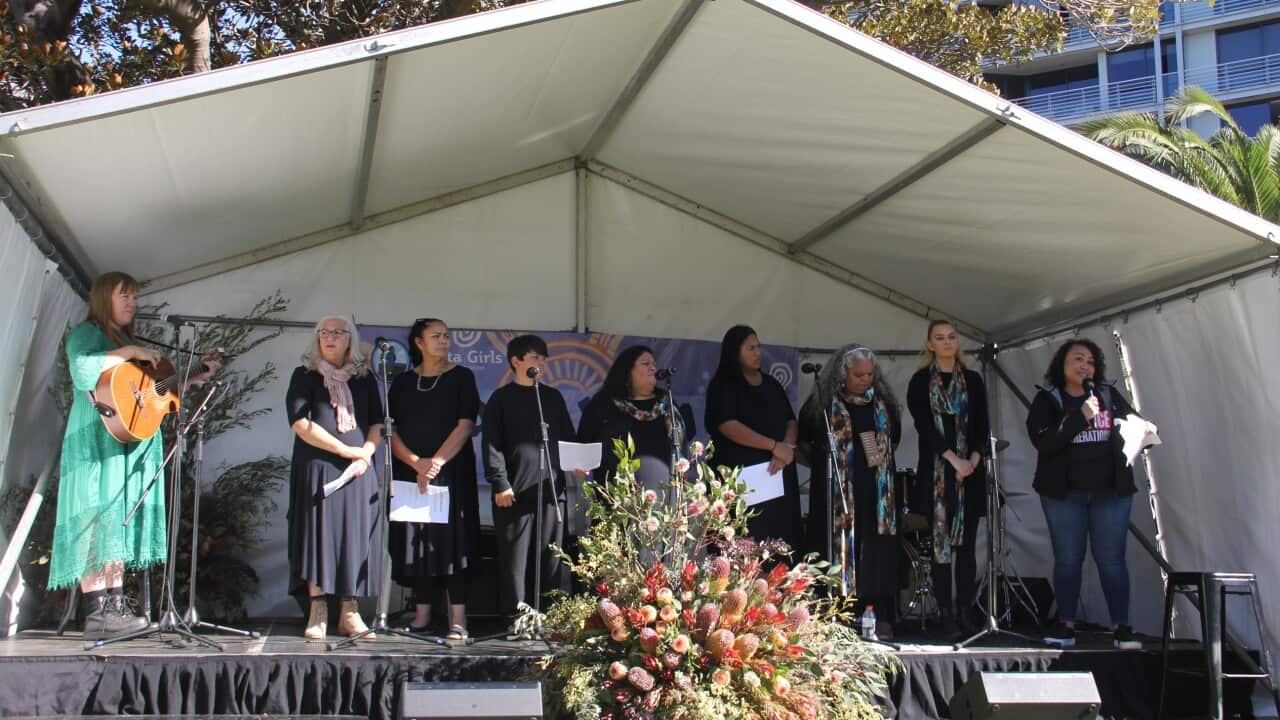 Nine women are standing on a stage under a white tent as part of a Reconciliation Week event.
