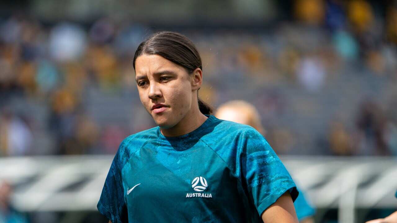 Woman in navy blue uniform with brown hair in ponytail has a serious expression on her face.