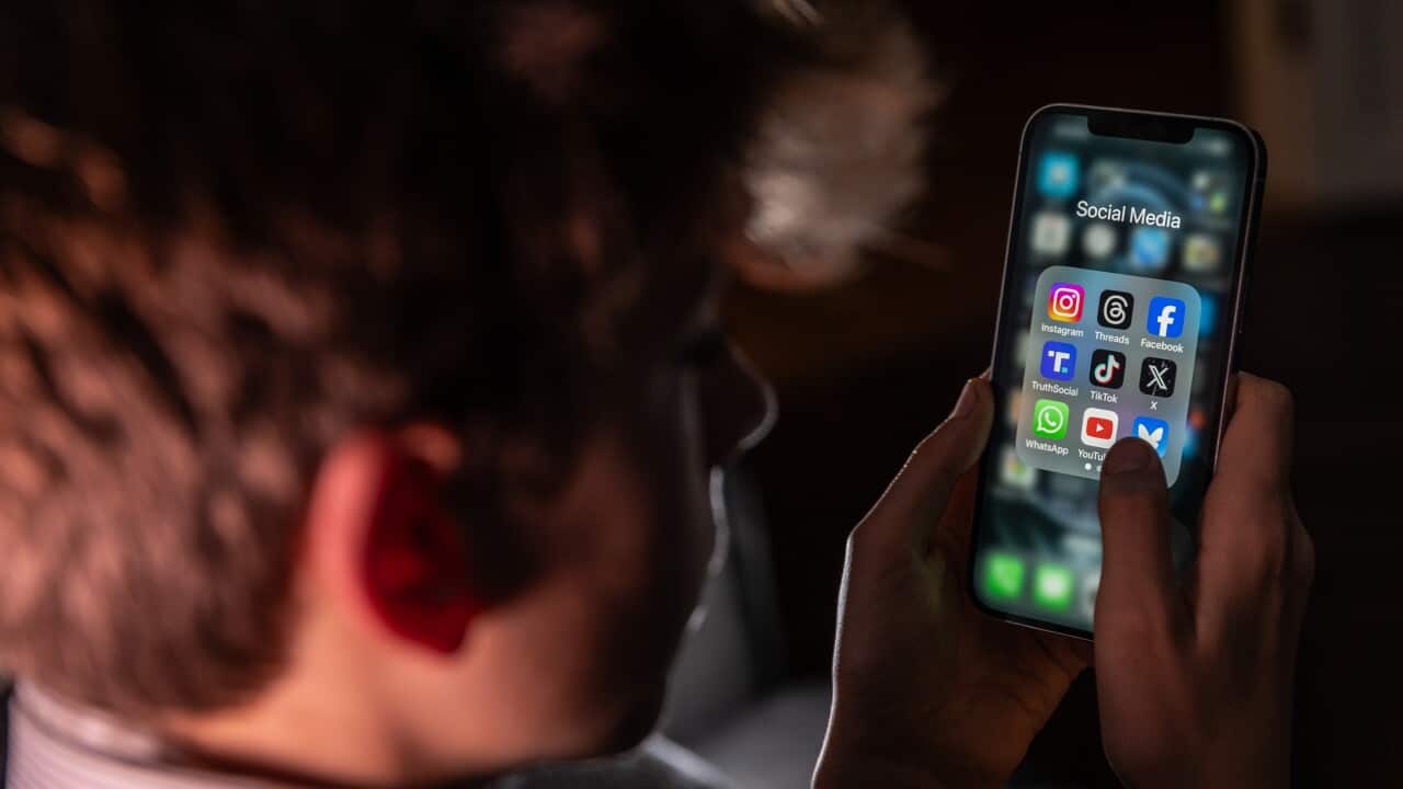 A young boy is looking at a phone with a selection of social media apps in a folder.