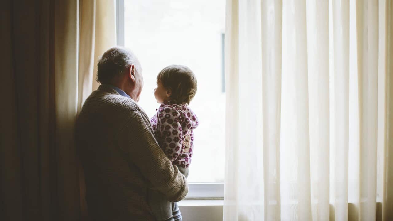 An older man stands with a child looking out of a window.