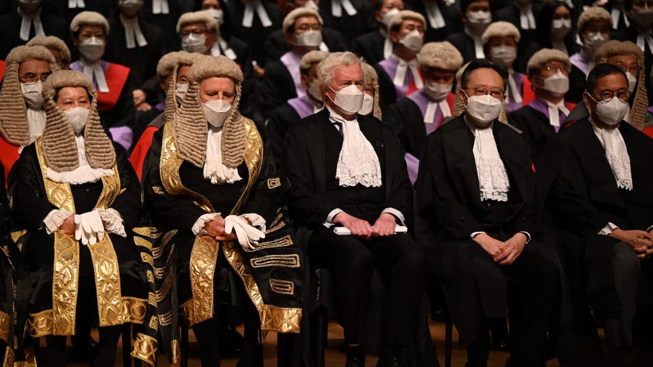 A group of judges, wearing masks and some wearing wigs, are seated in rows.