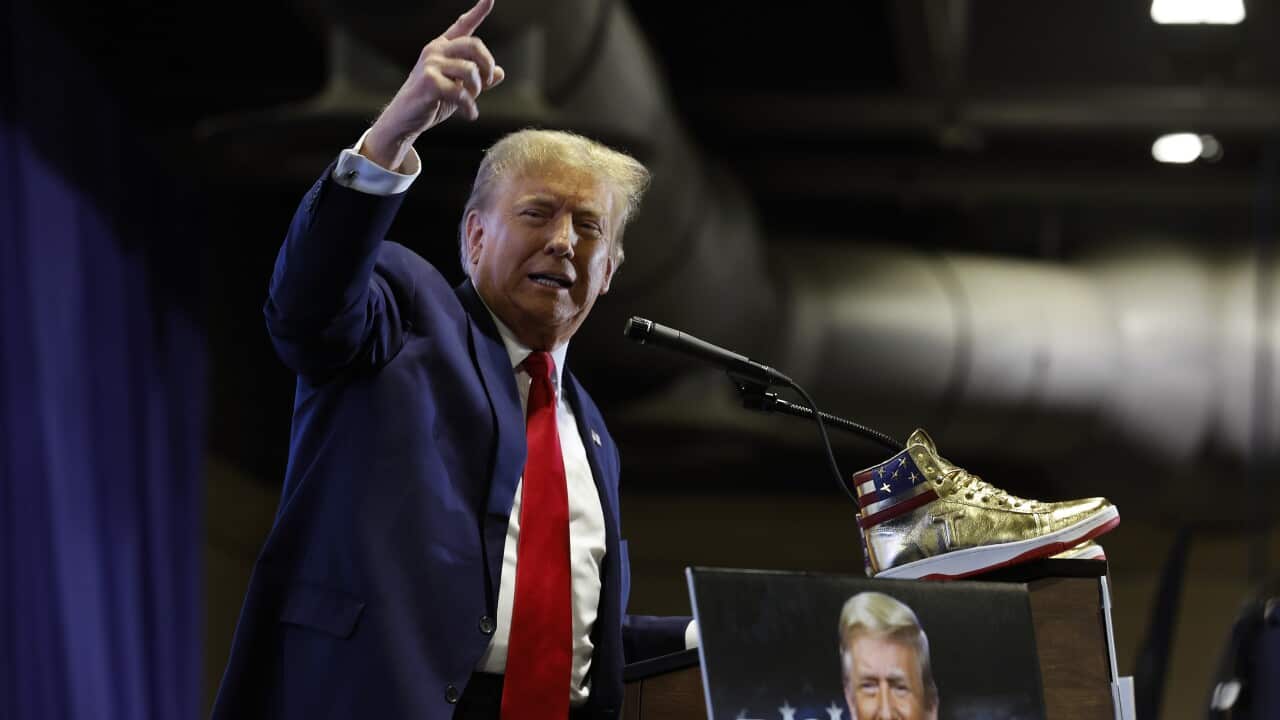 A man wearing a suit and tie standing in front of a lectern with a gold-coloured shoe sitting on it.
