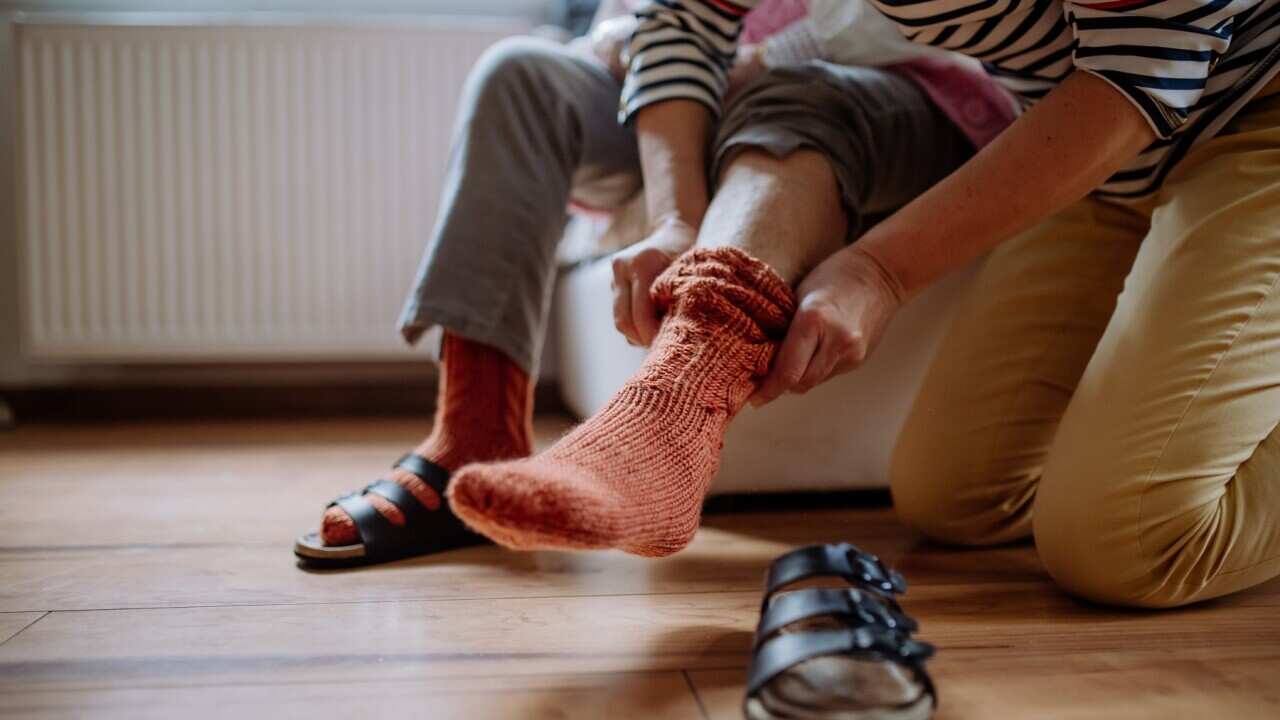 Close-up of healthcare worker putting on warm socks to senior woman.