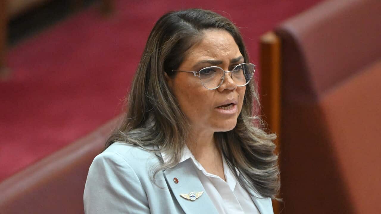 A woman in an aqua blue blazer is speaking in the Senate.