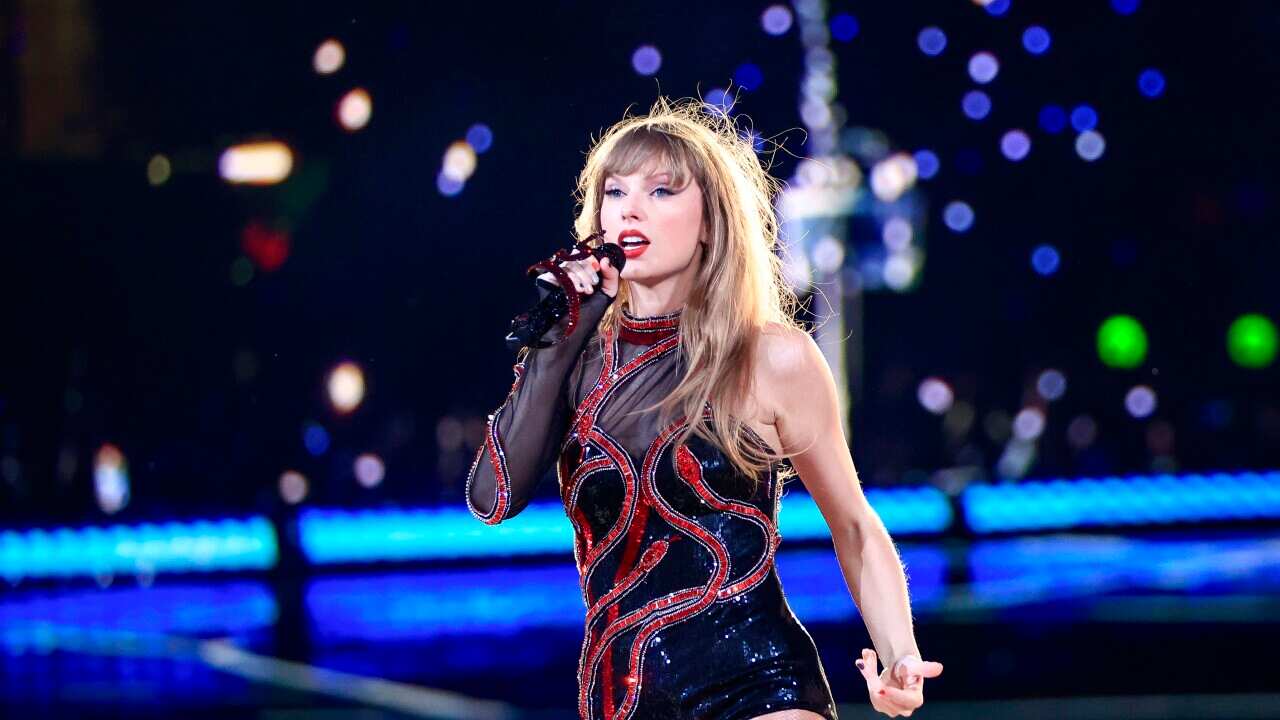 Taylor Swift holding a microphone and singing on stage.