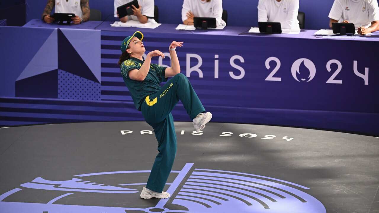A woman wearing a green and gold sports uniform performs a dance move