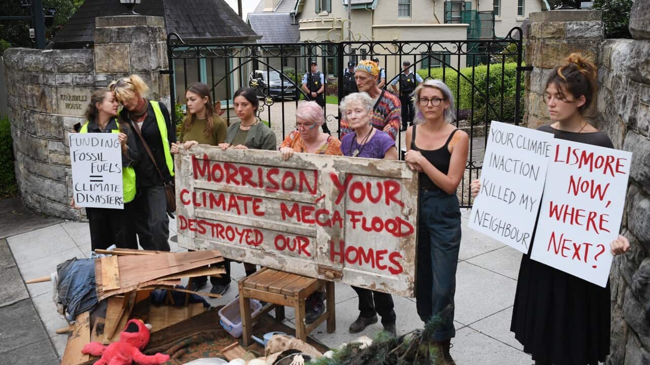 Protesters are seen holding placards and standing behind flood-damaged items out the front of the prime minister's residence.