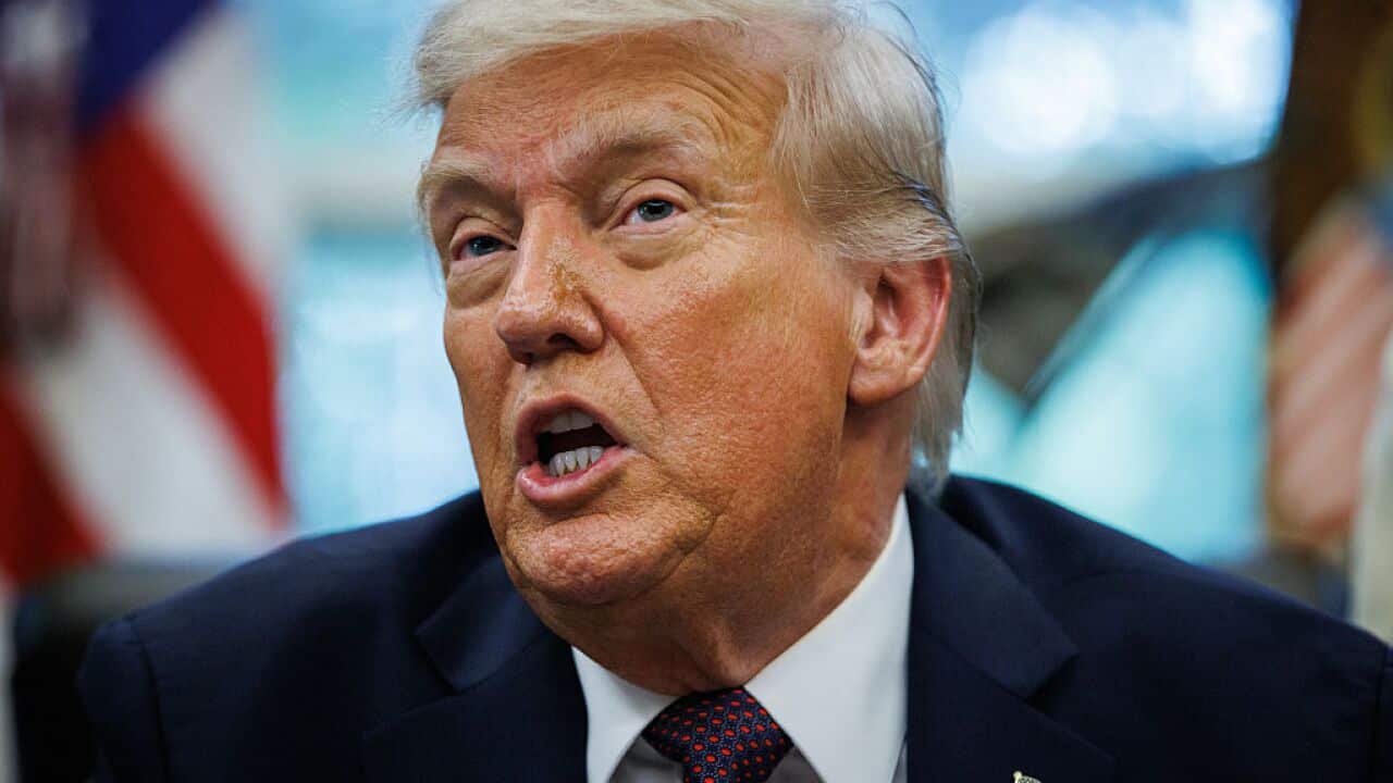 A close-up of Donald Trump as he talks, wearing a navy suit and a spotted red tie.