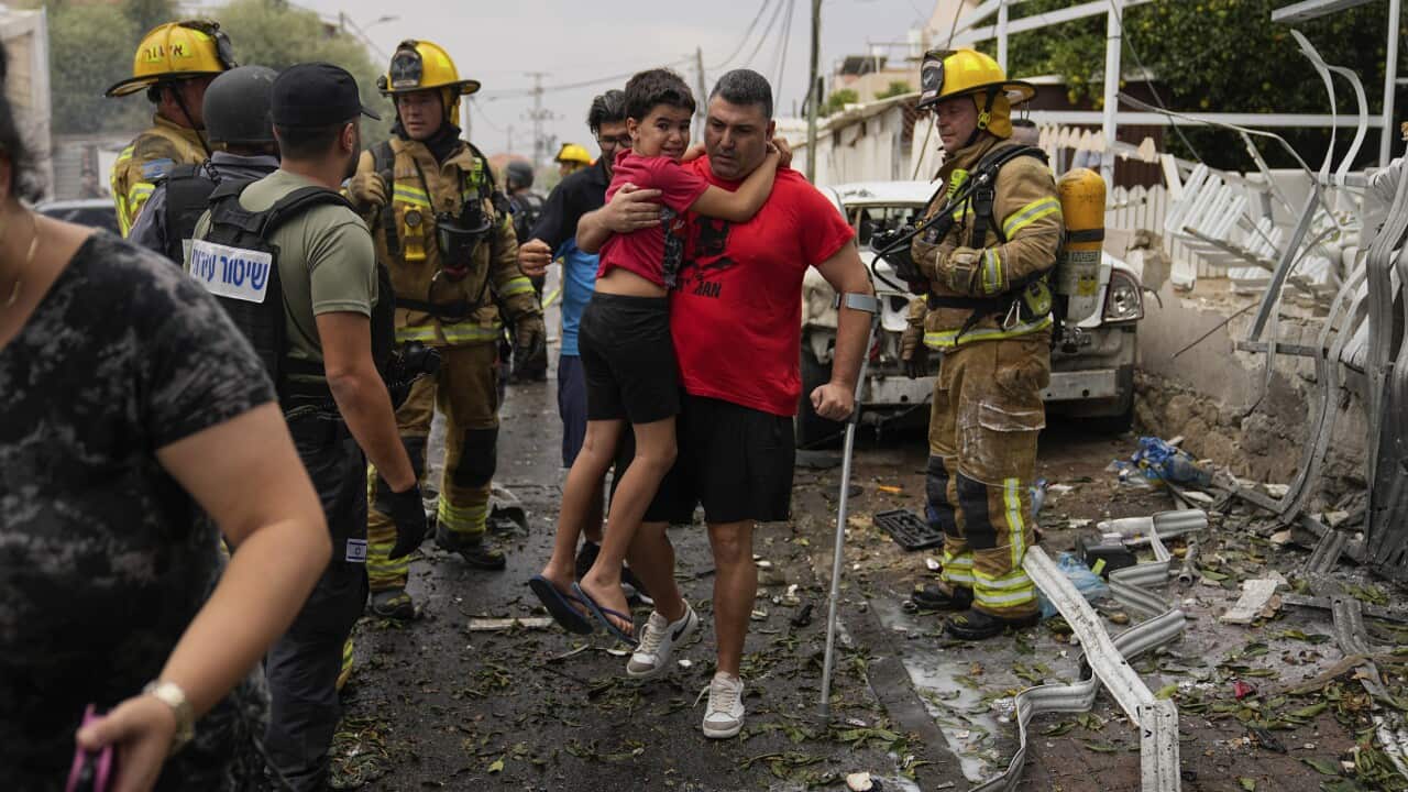 A man holds a child with building rubble around him
