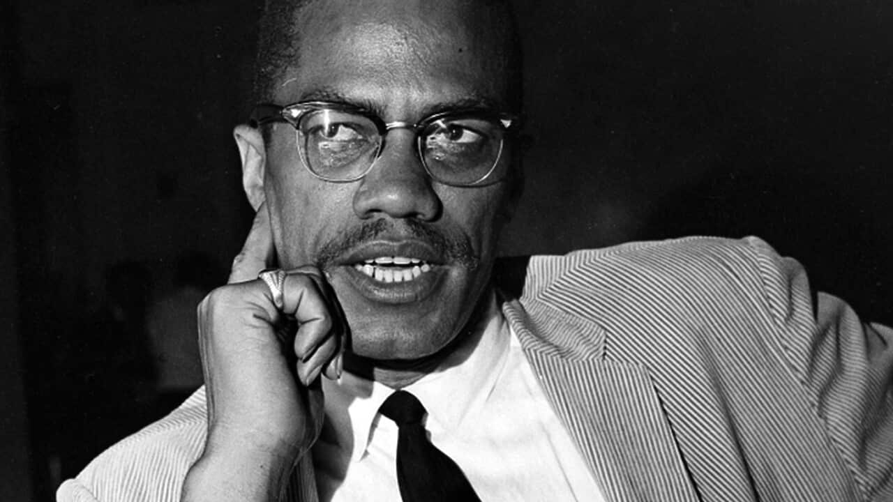 A black and white photo of a man speaking while seated.