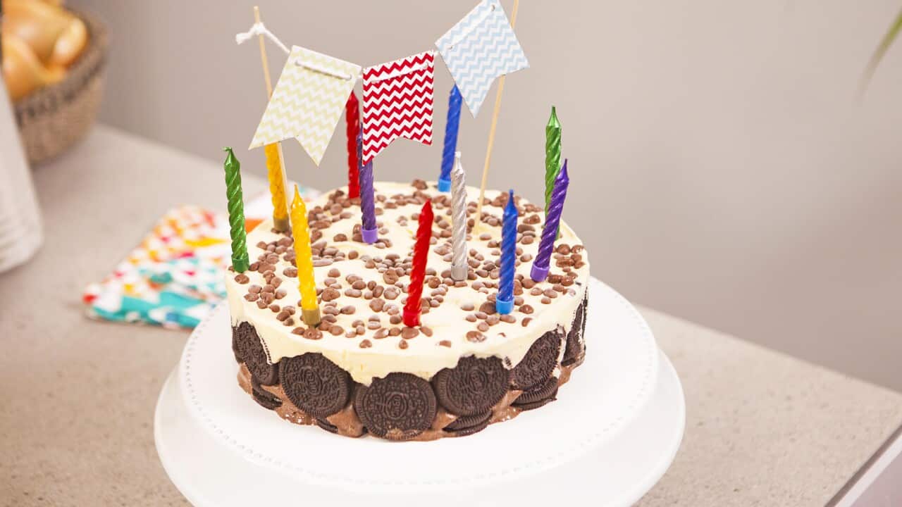 An ice-cream cake, with Oreo cookies lining the side, sits on a white plate. The cake is decorated with candles and mini bunting.