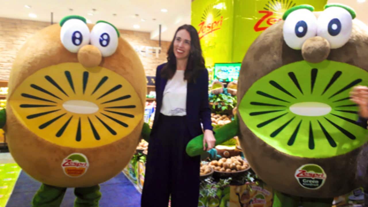 New Zealand Prime Minister Jacinda Ardern stands between two people dressed as kiwifruit.