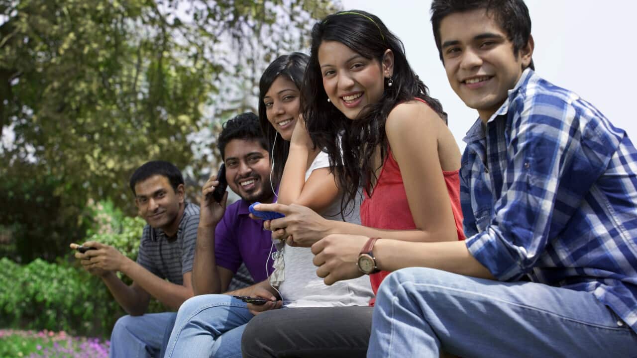 Portrait of smiling friends using cell phone in lawn