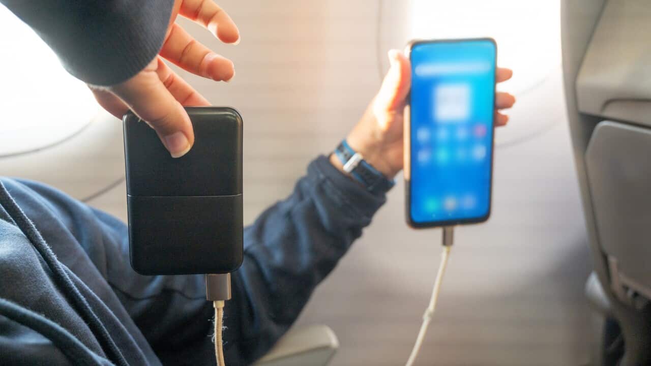 A child uses a mobile phone on a plane while charging with a power bank.