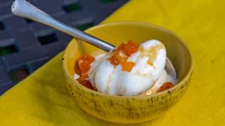 Two scoops of ice-cream, caramel sauce and chunks of soft dried fruit sit in a yellow bowl on a yellow tablecloth.