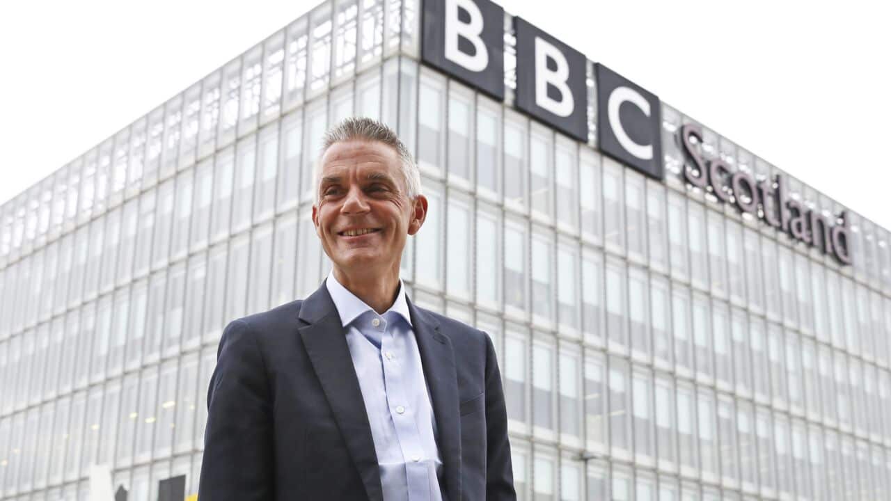A man in a suit stands in front of a building with a sign that reads 'BBC Scotland'