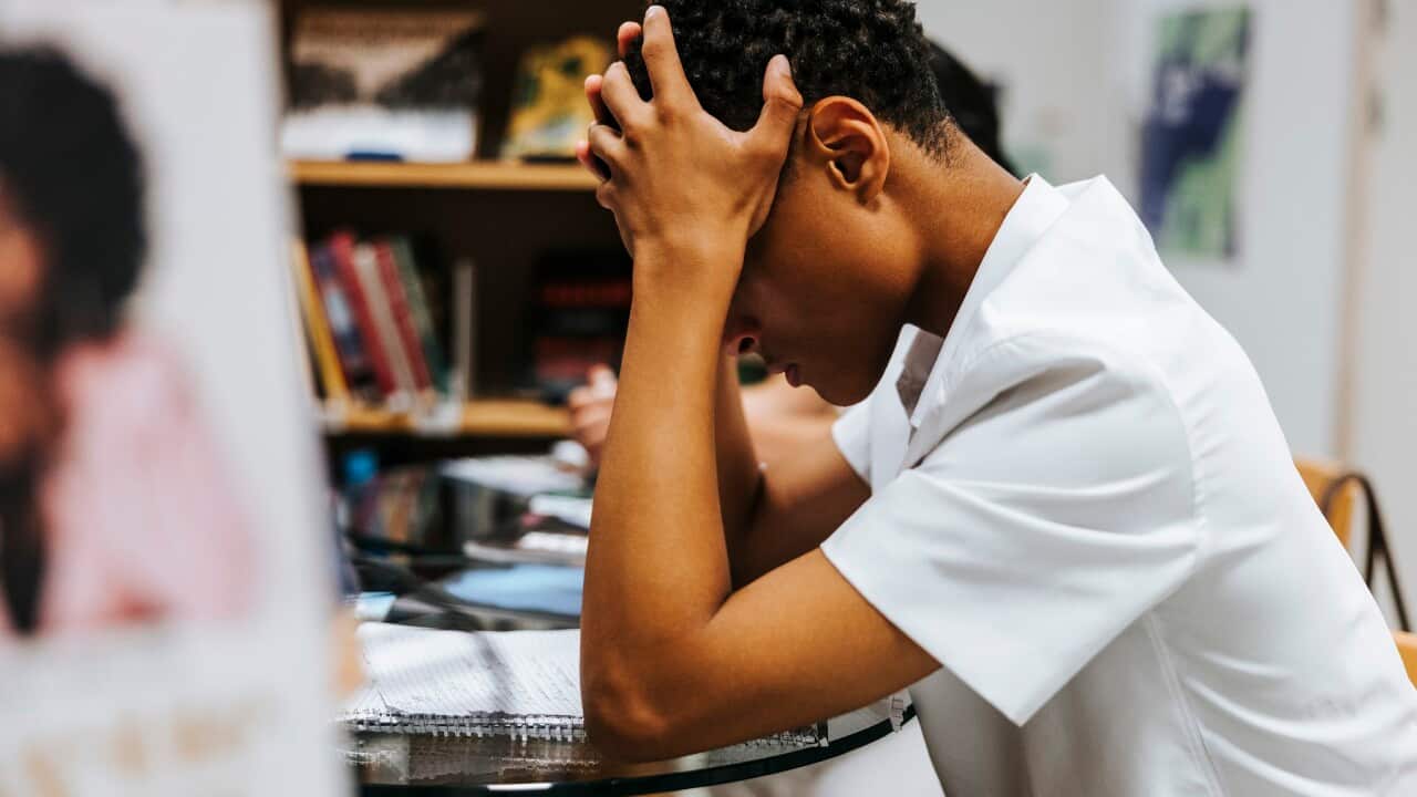Side view of stressed teenage boy sitting with head in hand at library of school