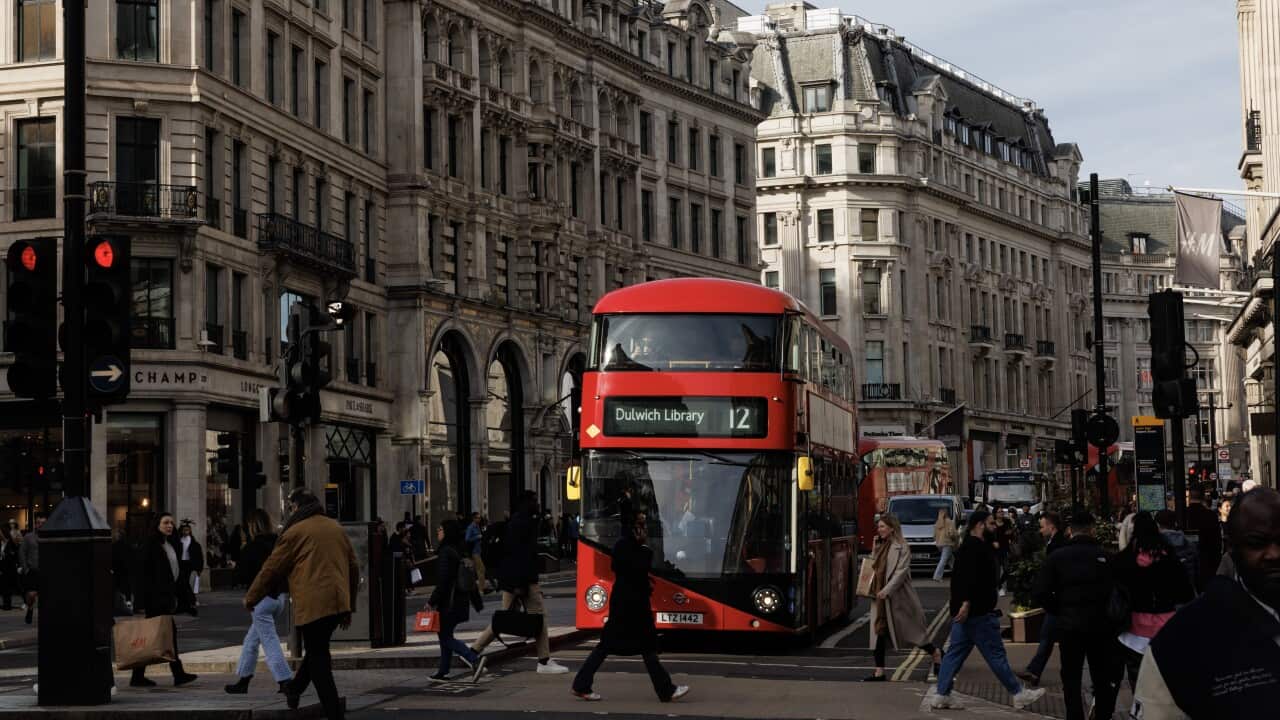 A double-decker bus in the middle of a bustling London street, with pedestrians walking around it.